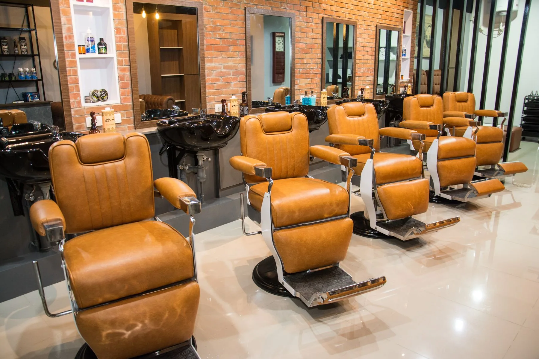 Deretan kursi barber kulit cokelat menghadap cermin.