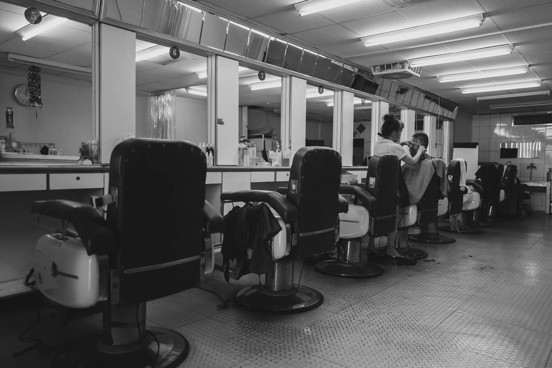Deretan cermin dan kursi barber dalam ruang monokrom.